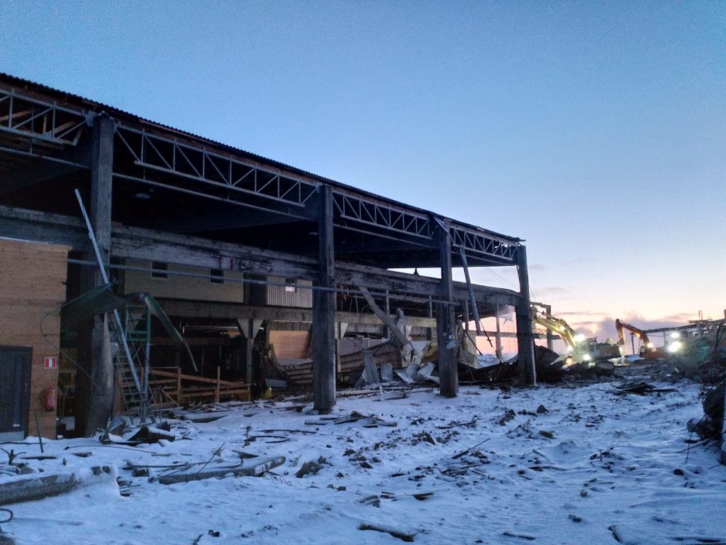 Teollisuushallin teräsrunko paljaana seinäverhouksen purun jälkeen iltavalossa